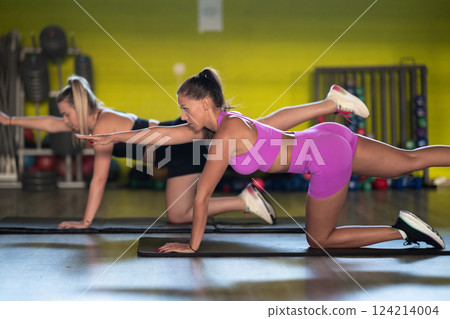 Two fitness women stretch together in the gym, supporting each other in their journey towards flexibility and wellness. 124214004