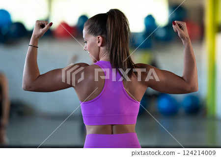 A fitness woman posing in the gym, proudly showing off her biceps and showcasing her strength and dedication to fitness. 124214009