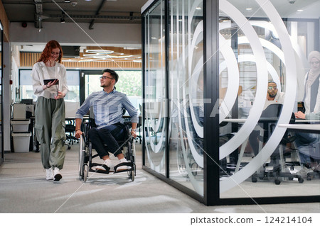 Business colleagues, collaborative business colleagues, including a person in a wheelchair, walk past a modern glass office corridor, illustrating diversity, teamwork and empowerment in the workplace. Business colleagues, collaborative business colleagues, including a person in a wheelchair, walk past a modern glass office corridor, illustrating diversity, teamwork and empowerment in the workplace. 124214104