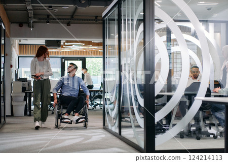 Business colleagues, collaborative business colleagues, including a person in a wheelchair, walk past a modern glass office corridor, illustrating diversity, teamwork and empowerment in the workplace. Business colleagues, collaborative business colleagues, including a person in a wheelchair, walk past a modern glass office corridor, illustrating diversity, teamwork and empowerment in the workplace. 124214113