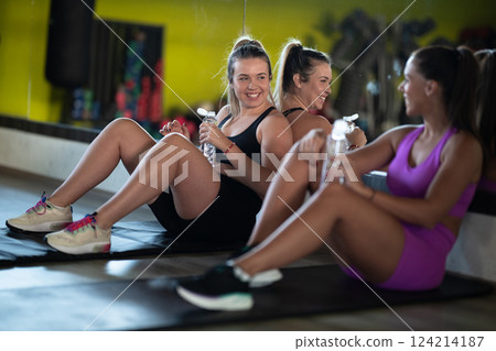 Two fitness women resting and recovering in the gym after an intense workout session, showcasing strength, endurance, and dedication to their fitness journey. Two fitness women resting and recovering in the gym after an intense workout session, showcasing strength, endurance, and dedication to their fitness journey. 124214187