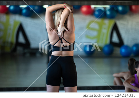 Two woman in the gym, one resting while the other stretches, recovering and recharging after an intense workout session. Two woman in the gym, one resting while the other stretches, recovering and recharging after an intense workout session. 124214333