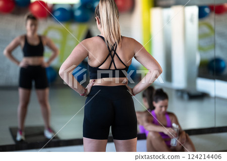 Two woman in the gym, one resting while the other stretches, recovering and recharging after an intense workout session. Two woman in the gym, one resting while the other stretches, recovering and recharging after an intense workout session. 124214406