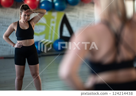 A fit and determined woman takes a short break during an intense workout session at the gym, showcasing strength and perseverance. A fit and determined woman takes a short break during an intense workout session at the gym, showcasing strength and perseverance. 124214438