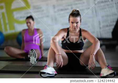 Two fitness women resting and recovering in the gym after an intense workout session, showcasing strength, endurance, and dedication to their fitness journey. Two fitness women resting and recovering in the gym after an intense workout session, showcasing strength, endurance, and dedication to their fitness journey. 124214442