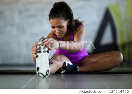 Woman Stretching in Gym. A athletic woman wearing a purple sports outfit is stretching her legs in a gym. 124214450