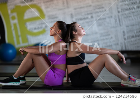 Two fitness women resting and recovering in the gym after an intense workout session, showcasing strength, endurance, and dedication to their fitness journey. Two fitness women resting and recovering in the gym after an intense workout session, showcasing strength, endurance, and dedication to their fitness journey. 124214586