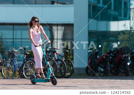 Elegant woman in a pink dress and sunglasses riding an electric scooter through the sunny city streets, embracing the freedom and style of a perfect urban adventure. Elegant woman in a pink dress and sunglasses riding an electric scooter through the sunny city streets, embracing the freedom and style of a perfect urban adventure. 124214592