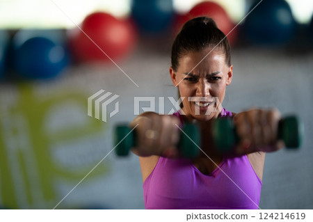 A focused and determined woman performs a strength building dumbbell workout at the gym, showcasing her athletic physique and dedication to fitness. A focused and determined woman performs a strength building dumbbell workout at the gym, showcasing her athletic physique and dedication to fitness. 124214619