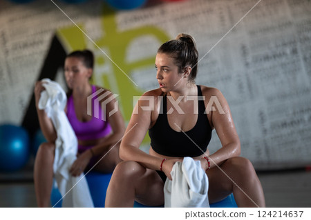 A beautiful and fit woman sitting on a gym ball with a towel, resting and recovering after an intense workout. A beautiful and fit woman sitting on a gym ball with a towel, resting and recovering after an intense workout. 124214637