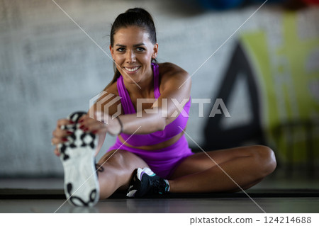 Woman Stretching in Gym. A athletic woman wearing a purple sports outfit is stretching her legs in a gym. 124214688