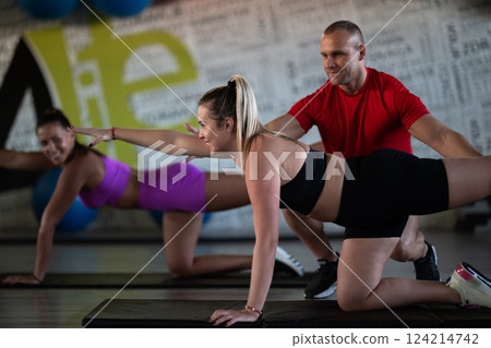 A trainer guides two women through stretching exercises in the gym, promoting flexibility, wellness, and a healthy lifestyle. 124214742