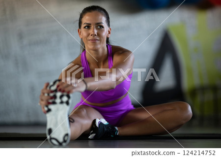Woman Stretching in Gym. A athletic woman wearing a purple sports outfit is stretching her legs in a gym. 124214752