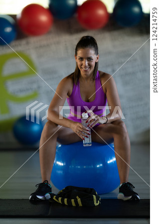 A fit woman takes a well deserved break in the gym, sipping water from her bottle after an intense workout session 124214759