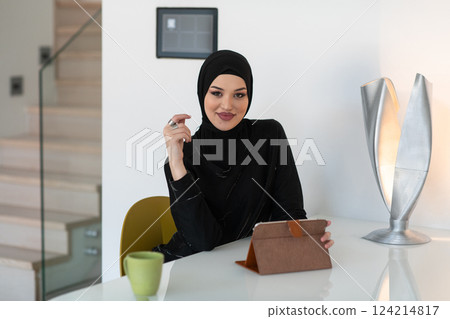 Modern Muslim woman in a hijab working on a tablet at home. Modern Muslim woman in a hijab working on a tablet at home. 124214817