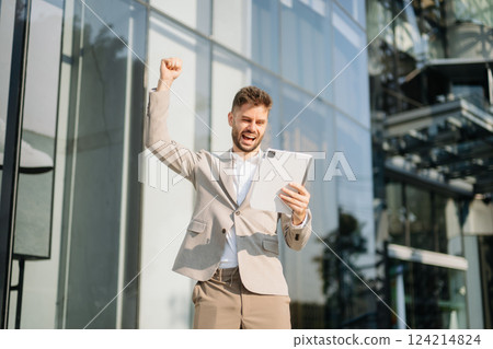 Handsome unshaven businessman walking with laptop, tablet and smartphone on city 124214824