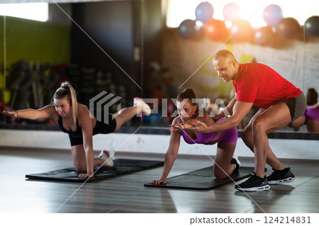 A trainer guides two women through stretching exercises in the gym, promoting flexibility, wellness, and a healthy lifestyle. 124214831