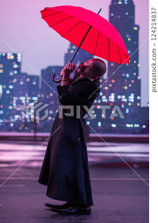Mysterious Clown Performer with Red Umbrella in Urban Nightscape. 124214837