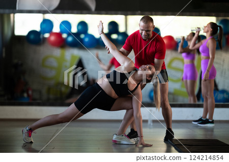 A trainer guides two women through stretching exercises in the gym, promoting flexibility, wellness, and a healthy lifestyle. 124214854