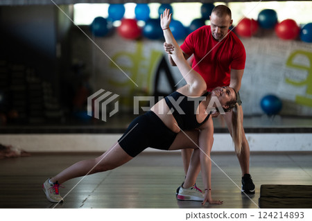 A trainer guides two women through stretching exercises in the gym, promoting flexibility, wellness, and a healthy lifestyle. 124214893
