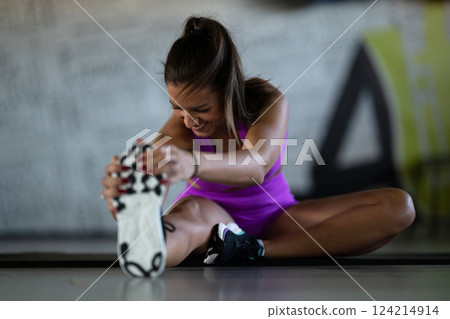 Woman Stretching in Gym. A athletic woman wearing a purple sports outfit is stretching her legs in a gym. 124214914