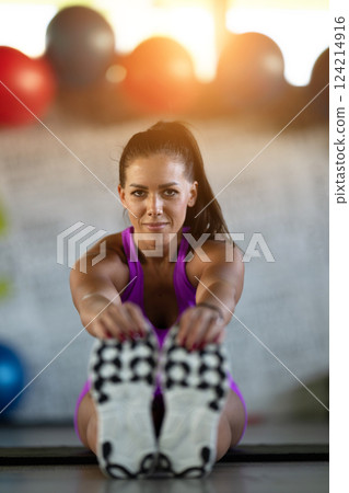Woman Stretching in Gym. A athletic woman wearing a purple sports outfit is stretching her legs in a gym. 124214916