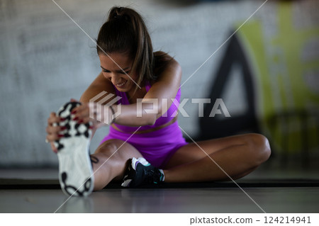 Woman Stretching in Gym. A athletic woman wearing a purple sports outfit is stretching her legs in a gym. Woman Stretching in Gym. A athletic woman wearing a purple sports outfit is stretching her legs in a gym. 124214941