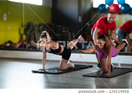 A trainer guides two women through stretching exercises in the gym, promoting flexibility, wellness, and a healthy lifestyle. 124214958