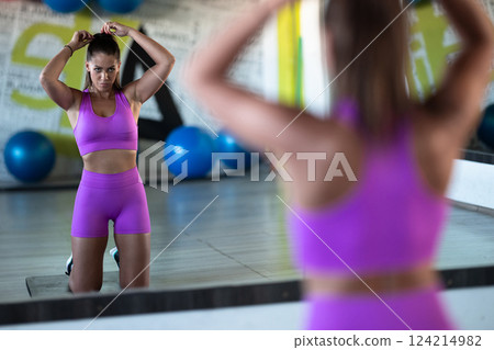A determined woman ties her hair in preparation for an intense workout, embodying focus and strength as she gears up for her fitness training session 124214982