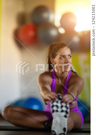 Woman Stretching in Gym. A athletic woman wearing a purple sports outfit is stretching her legs in a gym. Woman Stretching in Gym. A athletic woman wearing a purple sports outfit is stretching her legs in a gym. 124215001
