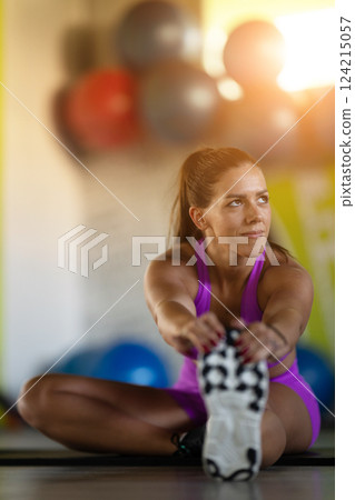 Woman Stretching in Gym. A athletic woman wearing a purple sports outfit is stretching her legs in a gym. Woman Stretching in Gym. A athletic woman wearing a purple sports outfit is stretching her legs in a gym. 124215057
