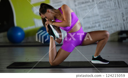 A woman stretches her body in the gym after an intense workout, a healthy muscle stretch after training. 124215059