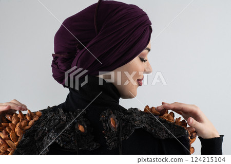 A stylish Muslim woman in a hijab presents her innovative handmade fashion accessory crafted from dried plums in a professional studio. 124215104