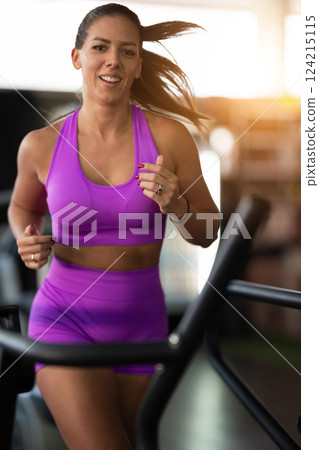 Woman Running on Treadmill in Gym.A fit woman wearing a purple sports outfit is running on a treadmill in a gym. She has a focused yet relaxed expression, with gym equipment and a warm light in the 124215115