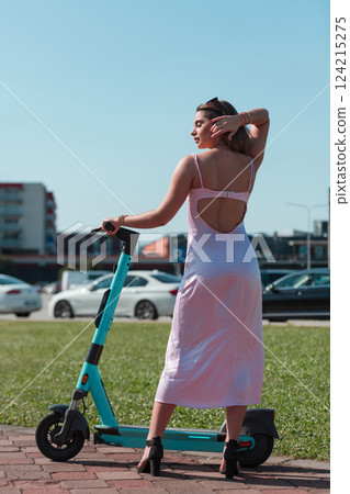 An elegant, stunning woman in a pink dress and sunglasses strikes a confident pose next to her electric scooter, radiating style and sophistication in the vibrant urban environment. An elegant, stunning woman in a pink dress and sunglasses strikes a confident pose next to her electric scooter, radiating style and sophistication in the vibrant urban environment. 124215275