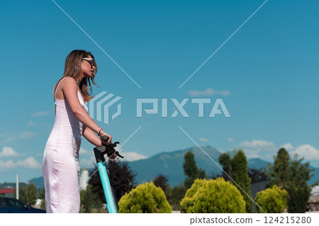Elegant woman in a pink dress and sunglasses riding an electric scooter through the sunny city streets, embracing the freedom and style of a perfect urban adventure. Elegant woman in a pink dress and sunglasses riding an electric scooter through the sunny city streets, embracing the freedom and style of a perfect urban adventure. 124215280