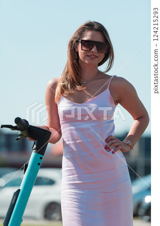 An elegant, stunning woman in a pink dress and sunglasses strikes a confident pose next to her electric scooter, radiating style and sophistication in the vibrant urban environment. An elegant, stunning woman in a pink dress and sunglasses strikes a confident pose next to her electric scooter, radiating style and sophistication in the vibrant urban environment. 124215293