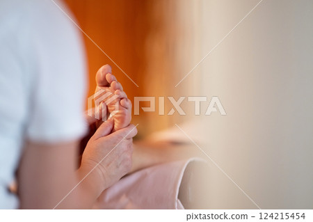 Foot Massage Therapy in a Relaxing Spa Setting. A professional massage therapist in a white uniform provides a soothing foot massage to a client in a calm and serene spa environment 124215454