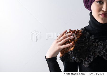 A stylish Muslim woman in a hijab presents her innovative handmade fashion accessory crafted from dried plums in a professional studio. 124215471