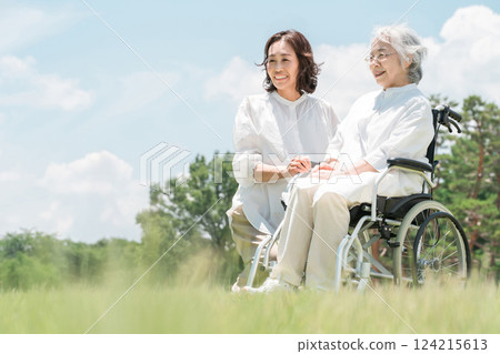 A senior woman in a wheelchair in a park and a woman assisting her (nursing care, parent and child, elderly care home) 124215613