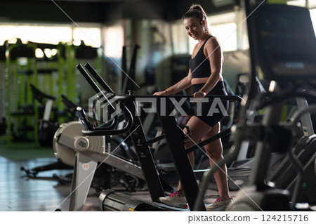 Woman Running on Treadmill in Gym.A fit woman wearing a purple sports outfit is running on a treadmill in a gym. She has a focused yet relaxed expression, with gym equipment and a warm light in the 124215716