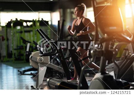 Woman Running on Treadmill in Gym.A fit woman wearing a purple sports outfit is running on a treadmill in a gym. She has a focused yet relaxed expression, with gym equipment and a warm light in the Woman Running on Treadmill in Gym.A fit woman wearing a purple sports outfit is running on a treadmill in a gym. She has a focused yet relaxed expression, with gym equipment and a warm light in the 124215721