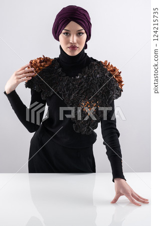 A stylish Muslim woman in a hijab presents her innovative handmade fashion accessory crafted from dried plums in a professional studio. A stylish Muslim woman in a hijab presents her innovative handmade fashion accessory crafted from dried plums in a professional studio. 124215735