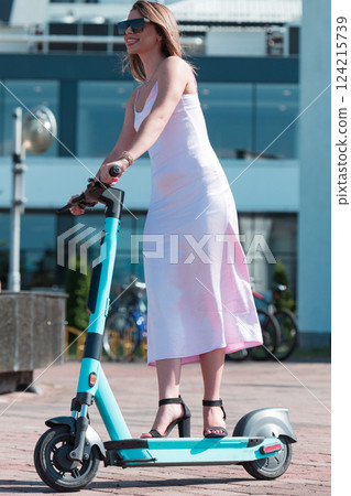 Elegant woman in a pink dress and sunglasses riding an electric scooter through the sunny city streets, embracing the freedom and style of a perfect urban adventure. Elegant woman in a pink dress and sunglasses riding an electric scooter through the sunny city streets, embracing the freedom and style of a perfect urban adventure. 124215739