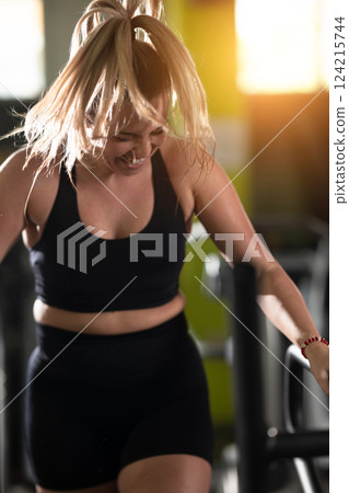 Woman Running on Treadmill in Gym.A fit woman wearing a purple sports outfit is running on a treadmill in a gym. She has a focused yet relaxed expression, with gym equipment and a warm light in the 124215744