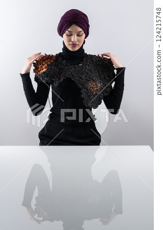 A stylish Muslim woman in a hijab presents her innovative handmade fashion accessory crafted from dried plums in a professional studio. 124215748