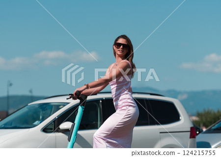 Elegant woman in a pink dress and sunglasses riding an electric scooter through the sunny city streets, embracing the freedom and style of a perfect urban adventure. 124215755