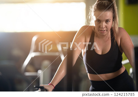 Woman Running on Treadmill in Gym.A fit woman wearing a purple sports outfit is running on a treadmill in a gym. She has a focused yet relaxed expression, with gym equipment and a warm light in the 124215785