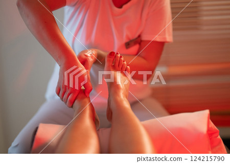 Foot Massage Therapy in a Relaxing Spa Setting. A professional massage therapist in a white uniform provides a soothing foot massage to a client in a calm and serene spa environment 124215790