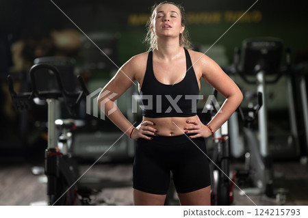 A fit woman strikes a confident pose in the gym after an intense workout, showcasing her strength, dedication, and progress. 124215793